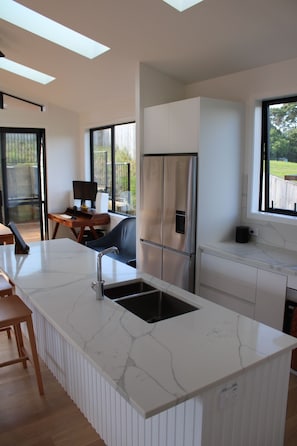 A modern kitchen with a marble countertop, stainless steel appliances, and a large window overlooking a deck.