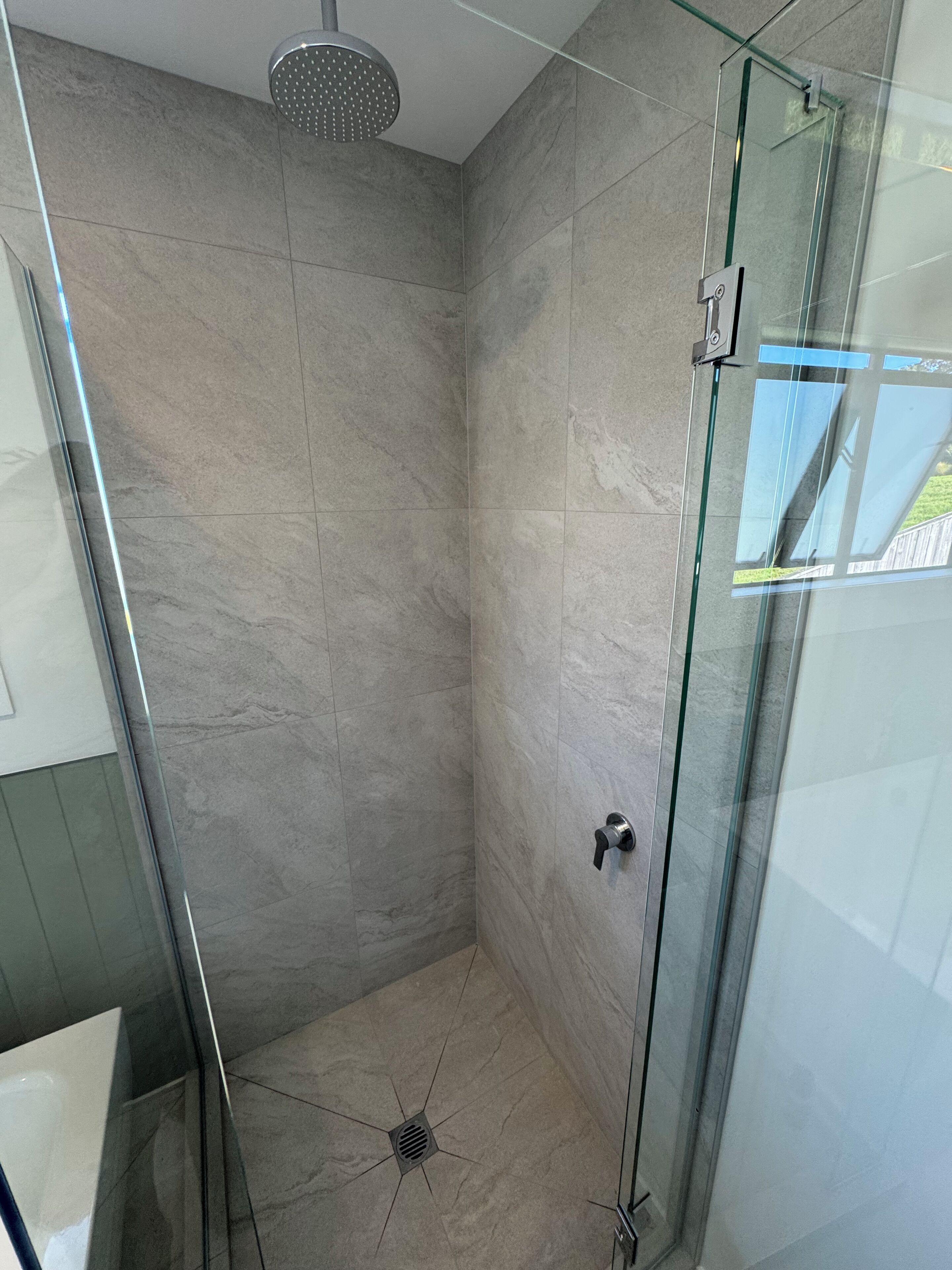 A glass-enclosed shower with a modern design, tiled walls, and a visible drain.
