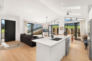 A modern kitchen with a central island, a dining area with a table and chairs, and a living space with a sofa. - New Bach 10 minutes walk from Langs Beach with 3 bdrm + 2 Bathrooms (Waipu)