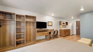 A compact bedroom with a bed, a desk, a TV, and a kitchenette. - Budget-Conscious Suite Near Top Austin Spots – Full Amenities for Long Stays (Austin)