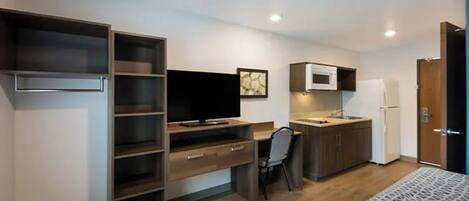A compact room with a bed, a desk with a chair, a television, a microwave, and a refrigerator.