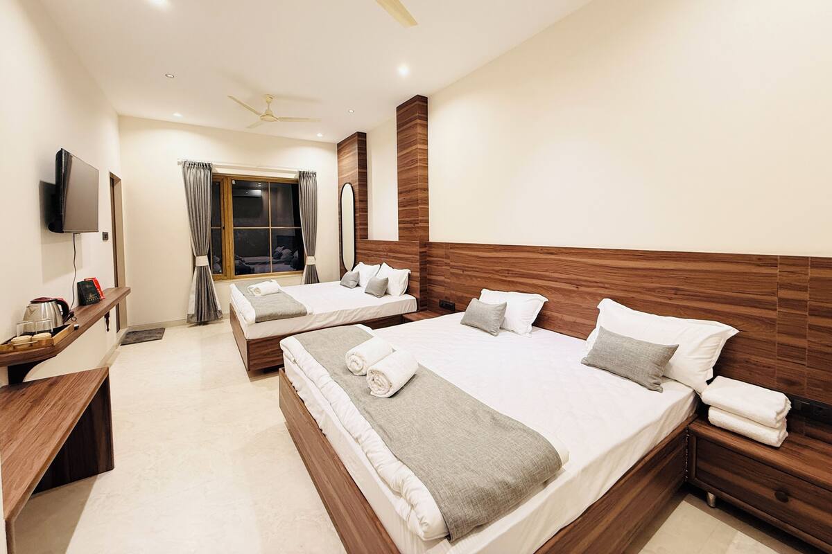A hotel room with two beds, a TV, a wooden headboard, and a window with curtains.