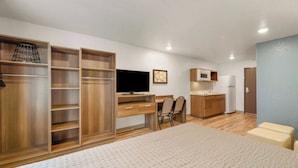 Ein kleines Schlafzimmer mit Bett, Schreibtisch, Fernseher und einer Küchenzeile.