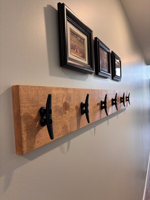A wooden wall-mounted rack with black hooks, above which are three framed pictures. - Brand New 2 Bedroom Lake Home in Charming Cumberland, WI (Cumberland)