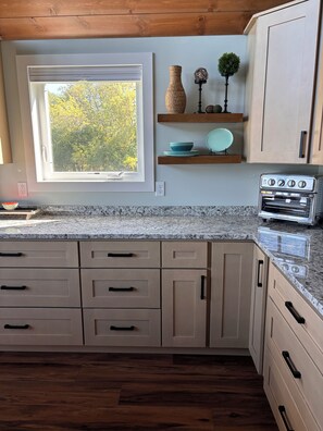 A kitchen with wooden cabinets, a built-in oven, a window with a view of trees, and a countertop with a bowl. - Brand New 3-Bedroom Lakefront Home with PICKLEBALL and PONTOON rental option (Cumberland)