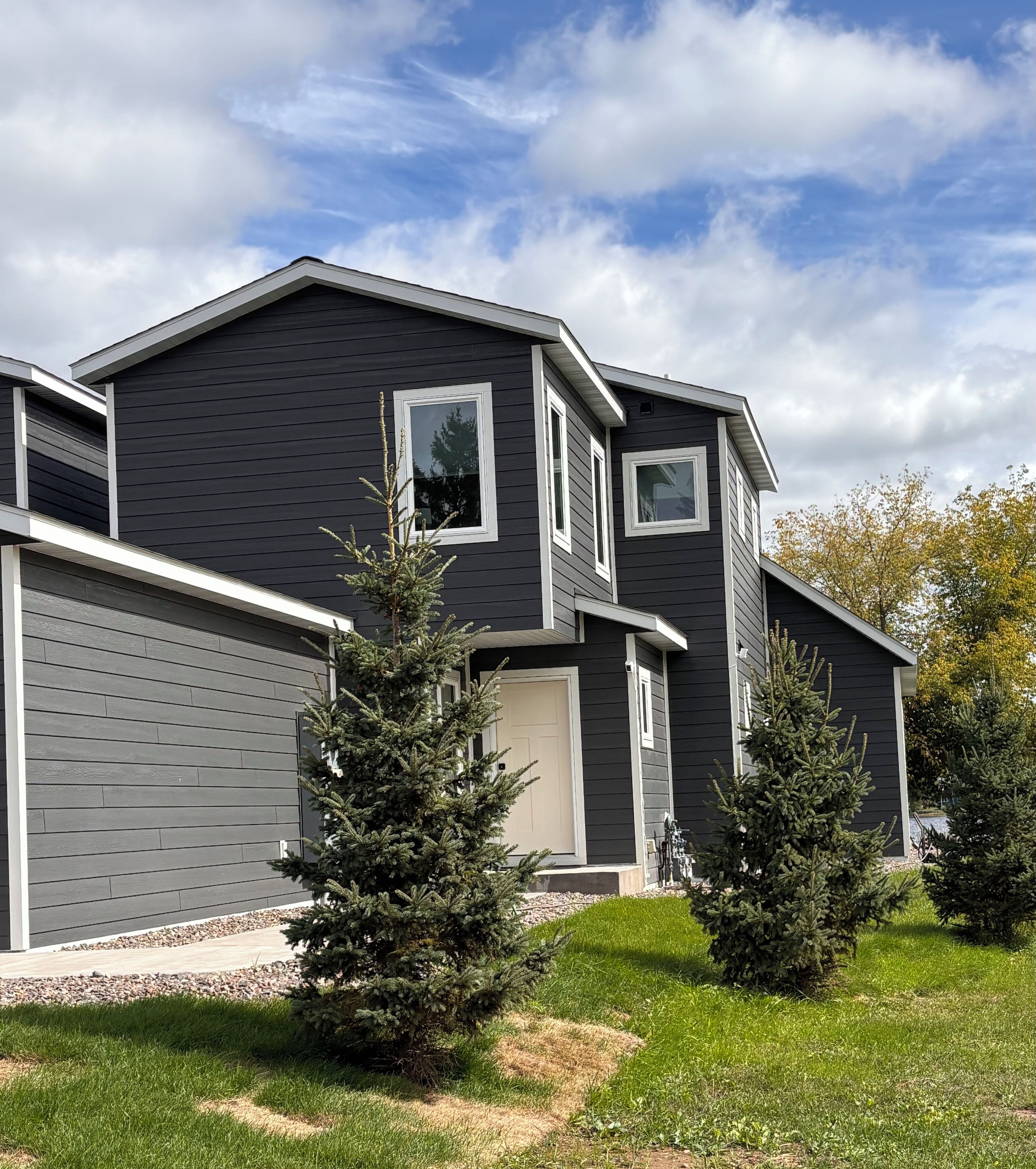 A modern two-story house with a dark exterior, a garage, and a well-maintained lawn with young trees.