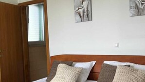 Een net opgemaakt bed met een opgevouwen handdoek, een houten hoofdbord en twee aan de muur bevestigde kunstwerken.