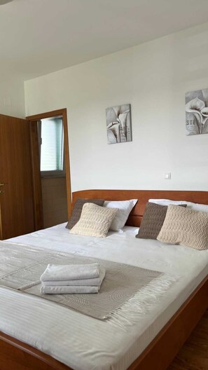 Ein ordentlich bezogenes Bett mit einem gefalteten Handtuch, einem Holz-Kopfteil und zwei an der Wand hängenden Kunstwerken.