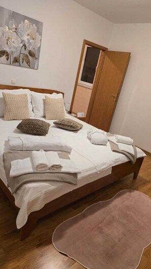 Ein ordentlich bezogenes Bett mit Kissen und gefalteten Handtüchern, eine Holztür und ein Bild an der Wand.