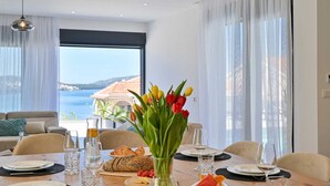 A dining area with a table set for two, a vase of tulips, and a view of the sea. - Luxury Villa Oasis with pool and jacuzzi near beach (Trogir)