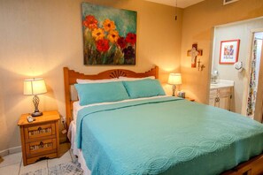 A bedroom with a bed, two bedside lamps, a wooden nightstand, a painting, a door with a mirror, and a small cabinet. - Sonoran Spa W102 Ground Floor 2BR/2ba (Puerto Peñasco)