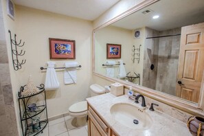 A bathroom with a large mirror, a toilet, a sink with a marble countertop, and two framed artworks on the wall. - Sonoran Spa W102 Ground Floor 2BR/2ba (Puerto Peñasco)