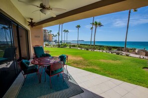 A balcony with a table and chairs, overlooking a grassy area with palm trees and a view of the ocean. - Sonoran Spa W102 Ground Floor 2BR/2ba (Puerto Peñasco)