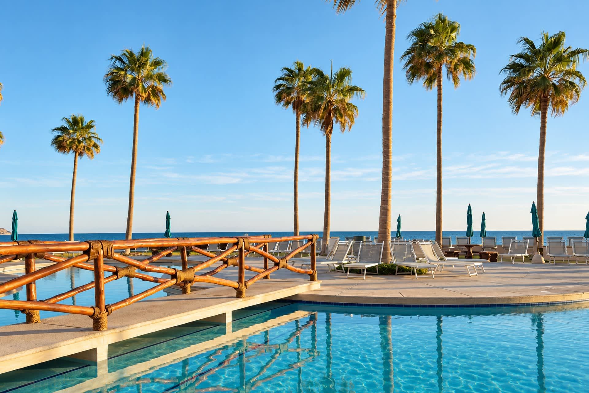 Área da piscina com cadeiras de sol e um guarda-corpo de bambu com vista para o mar.