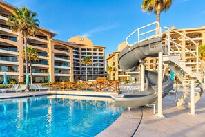 A hotel pool with a water slide, palm trees, and a multi-story building with balconies. - Sonoran Spa W102 Ground Floor 2BR/2ba (Puerto Peñasco)