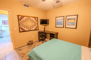 A hotel room with a bed, desk, chair, television, and two framed pictures on the wall. - Sonoran Spa W102 Ground Floor 2BR/2ba (Puerto Peñasco)