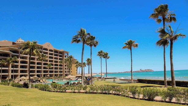 Een hotel met een zwembad, palmbomen en uitzicht op de oceaan.