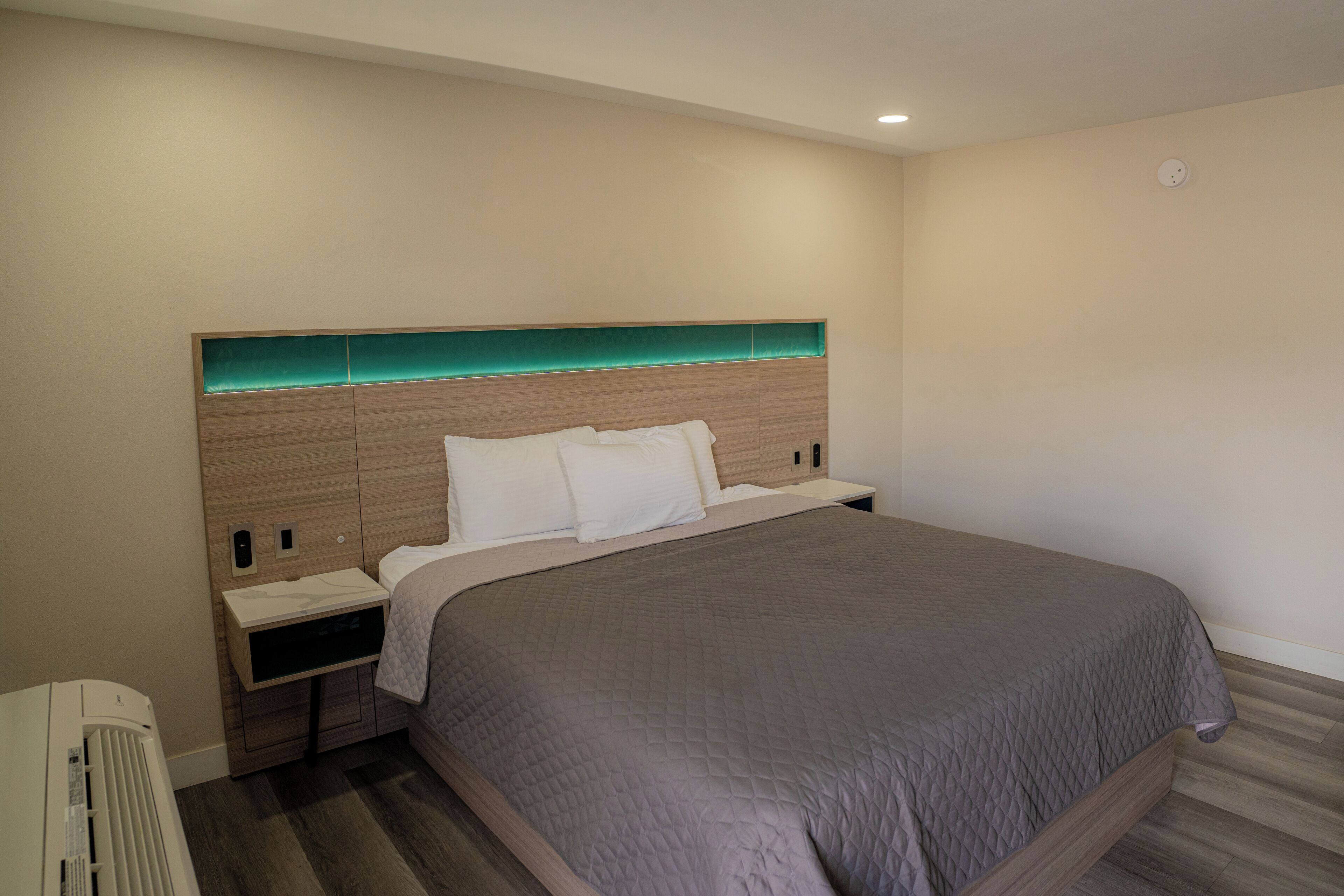 A modern hotel room with a large bed, a nightstand, and a built-in heater.