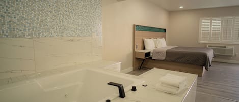 A modern bathroom with a large bathtub, a shower area, and a bed with a wooden headboard.