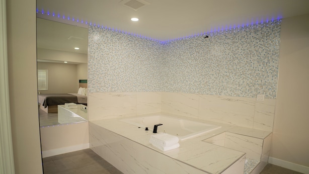 Ein modernes Badezimmer mit einer großen Badewanne, einem Spiegel und einer gefliesten Wand.