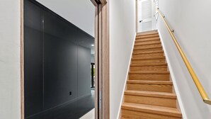 Een moderne trap met houten treden en een gele leuning, leidend naar een kamer met een zwarte muur en een witte deur.