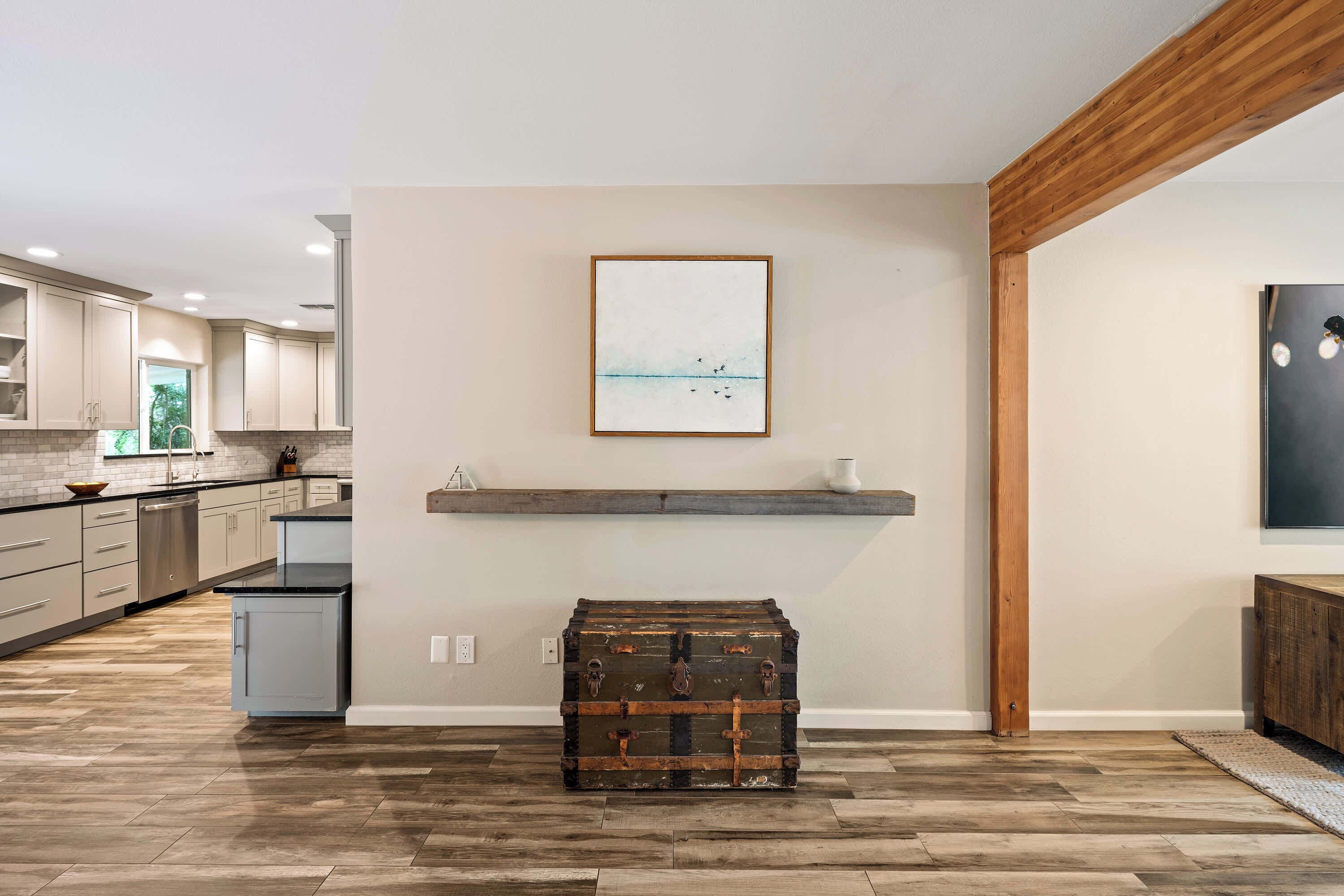 A modern kitchen with wooden flooring, a mounted artwork, and a vintage trunk.