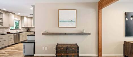 A modern kitchen with wooden flooring, a mounted artwork, and a vintage trunk.
