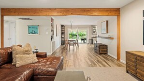 Amplia sala de estar con sofá de cuero, vigas de madera, una mesa de comedor y cocina al fondo.