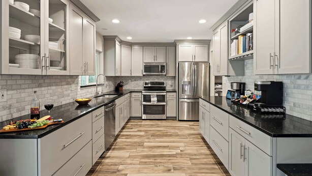 Una cocina moderna con armarios blancos, encimera negra y suelo de madera.