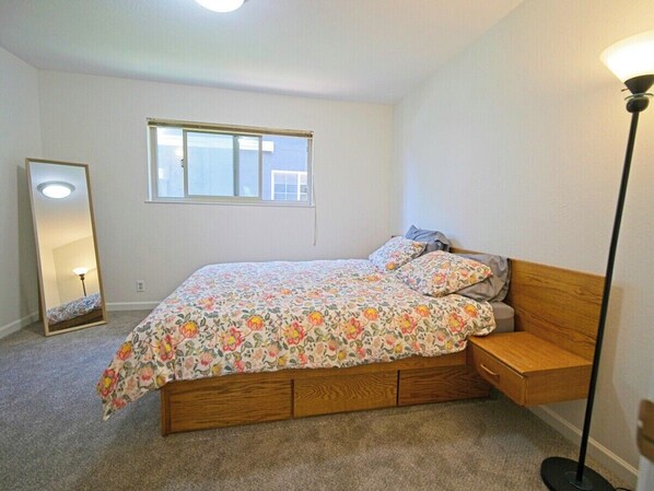A bedroom with a bed, a nightstand, a mirror, and a window.