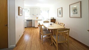 Un coin repas avec une table et des chaises en bois, une cuisine en arrière-plan et des tableaux encadrés accrochés aux murs.