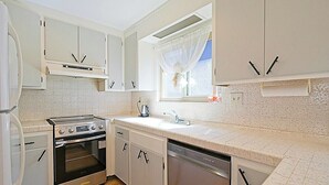 Une cuisine équipée d’un four encastré, d’un lave-vaisselle et d’une fenêtre ornée d’un rideau léger.