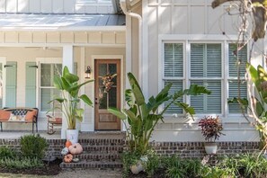 A house with a porch, a bench, and potted plants. - Coastal Luxury Retreat - Private Pool, Walk to the Pier, & Sleeps 16! (St. Simons Island)