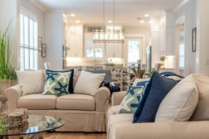 A modern living room with a beige sofa, a glass coffee table, and decorative pillows. - Coastal Luxury Retreat - Private Pool, Walk to the Pier, & Sleeps 16! (St. Simons Island)