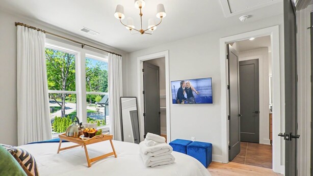 Ett hotellrum med en säng, en tv, ett fönster med gardiner, ett bricka med handdukar och en vattenkokare samt en dörr som leder till ett annat rum.