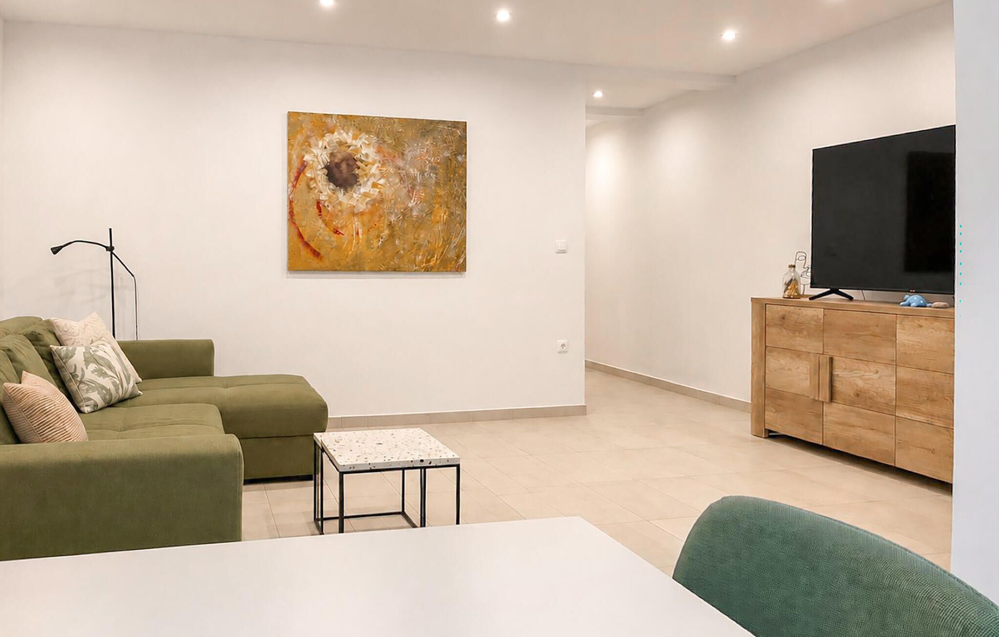 Una sala de estar moderna con un sofá verde, una mesita, un mueble con televisor y un cuadro abstracto grande en la pared.
