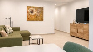 A modern living room with a green sofa, a small table, a cabinet with a TV, and a large abstract painting on the wall. - 1 bedroom cozy apartment in Vir (Vir)
