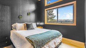 Ein Schlafzimmer mit einem großen Bett, einem Fenster mit Blick, einer dunklen Wand und einer Holzbalkendecke.
