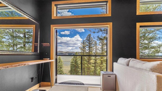 Ein modernes Interieur mit einer Couch, einem kleinen Tisch und Blick auf Bäume und Berge durch große Fenster.