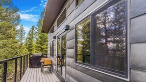 Eine Terrasse mit Grill, Stühlen und Tisch, mit Blick auf ein bewaldetes Gebiet.