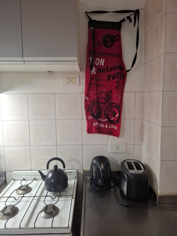 A kitchen with a gas stove, kettle, toaster, and a red banner on the wall.