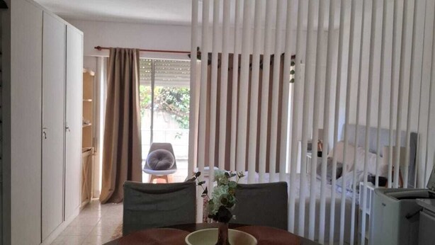 Uma sala de jantar com ventilador de teto, mesa e cadeiras, um arranjo de plantas e vista pela janela com cortinas.