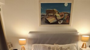 Cama bem arrumada com manta texturizada, duas luminárias de cabeceira e um quadro acima da cabeceira.