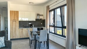 Cozinha moderna com armários brancos, área de refeições com cadeiras cinzas e uma janela grande com cortinas.