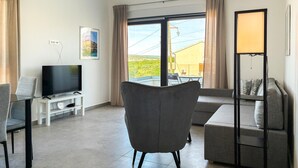 Sala de estar com televisão de tela plana, sofá, poltrona e luminária de chão.