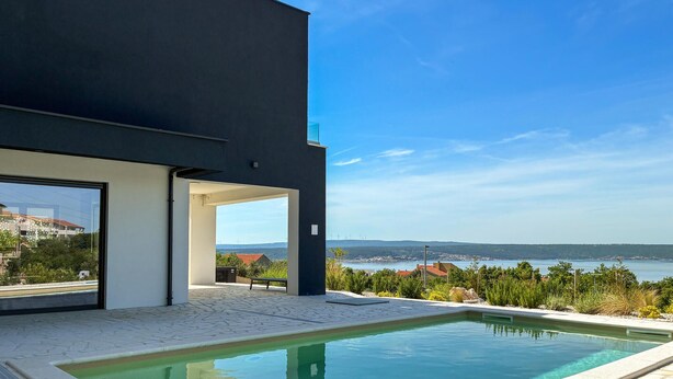 Um edifício moderno com piscina, grandes janelas e vista para um corpo d'água e paisagem distante.
