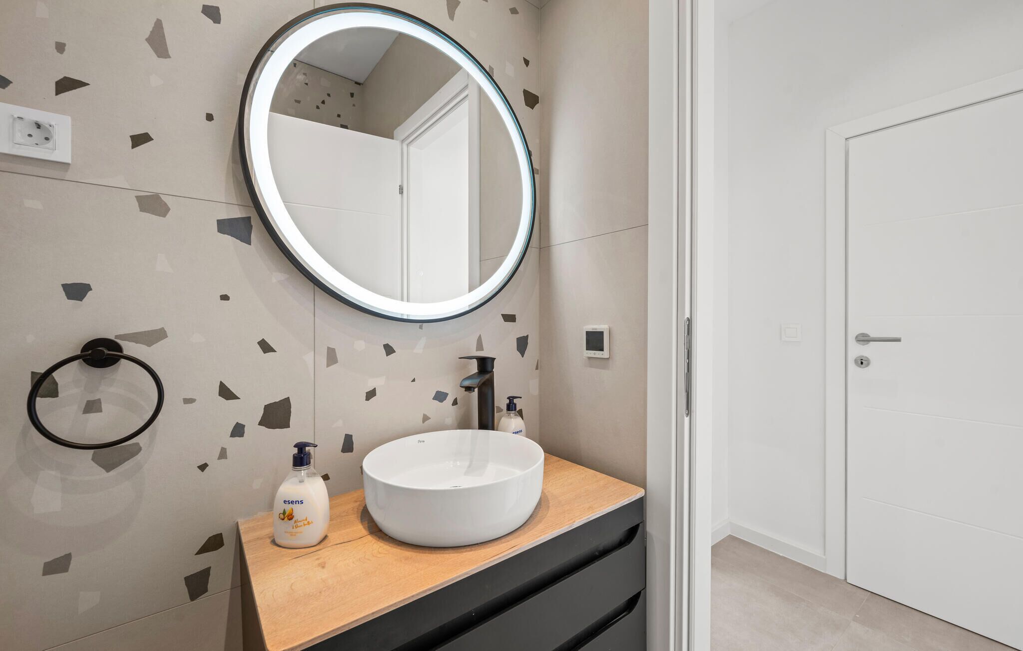 A bathroom with a round mirror, white sink, and a wooden vanity.