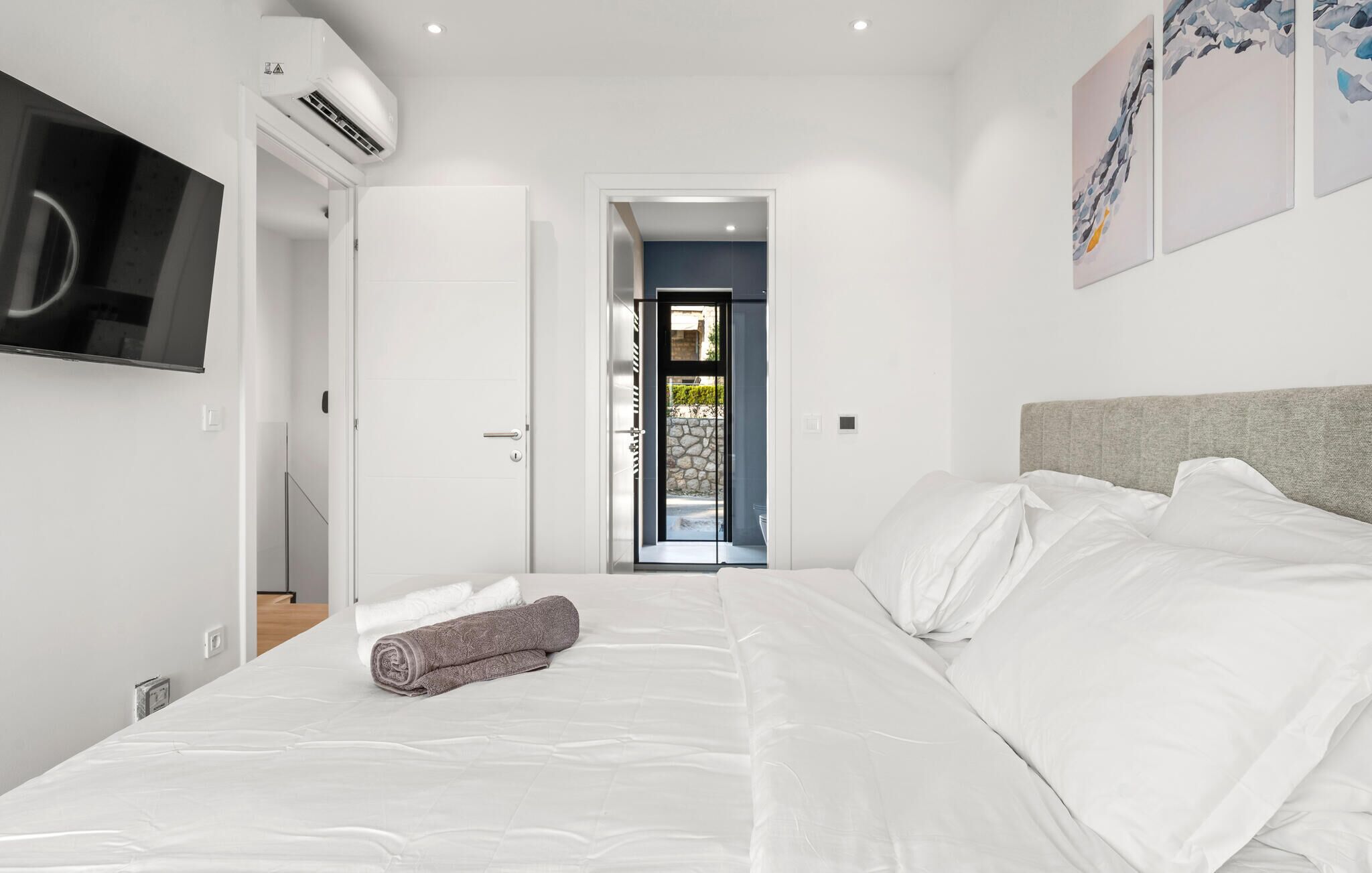 A modern hotel room with a bed, a television, and a door leading to a balcony.