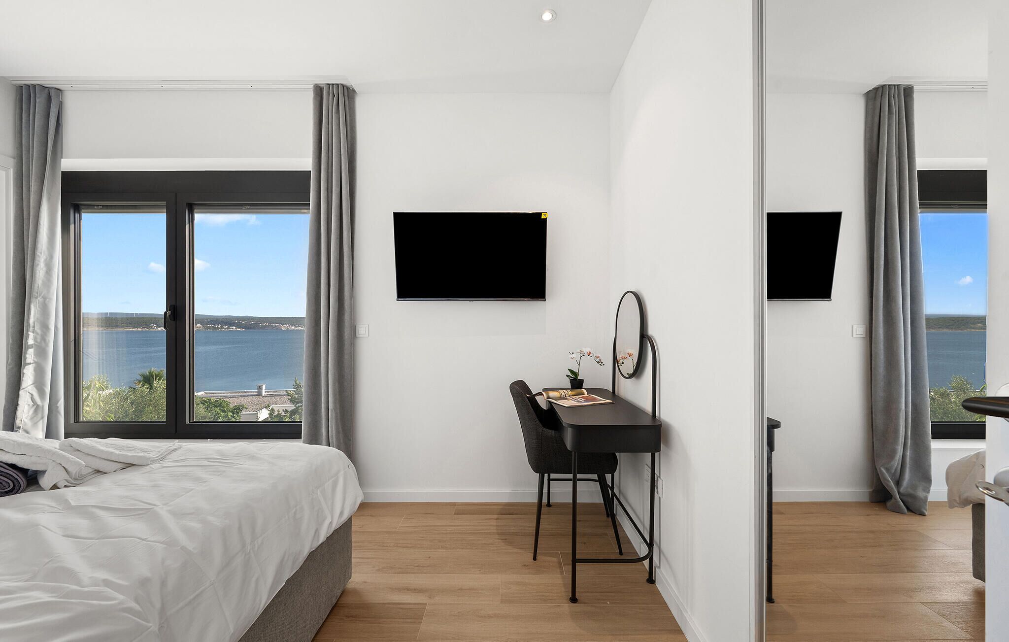 Ein Schlafzimmer mit Bett, Schreibtisch, Stuhl, Flachbildfernseher und Meerblick.