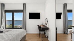 Ett sovrum med en säng, ett skrivbord, en stol, en platt-TV och utsikt över havet.